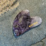 Zoom sur une pierre de gua sha améthyste disposée sur une pierre de granit