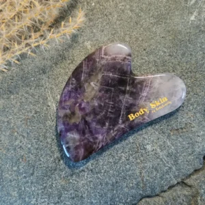 Zoom sur une pierre de gua sha améthyste disposée sur une pierre de granit