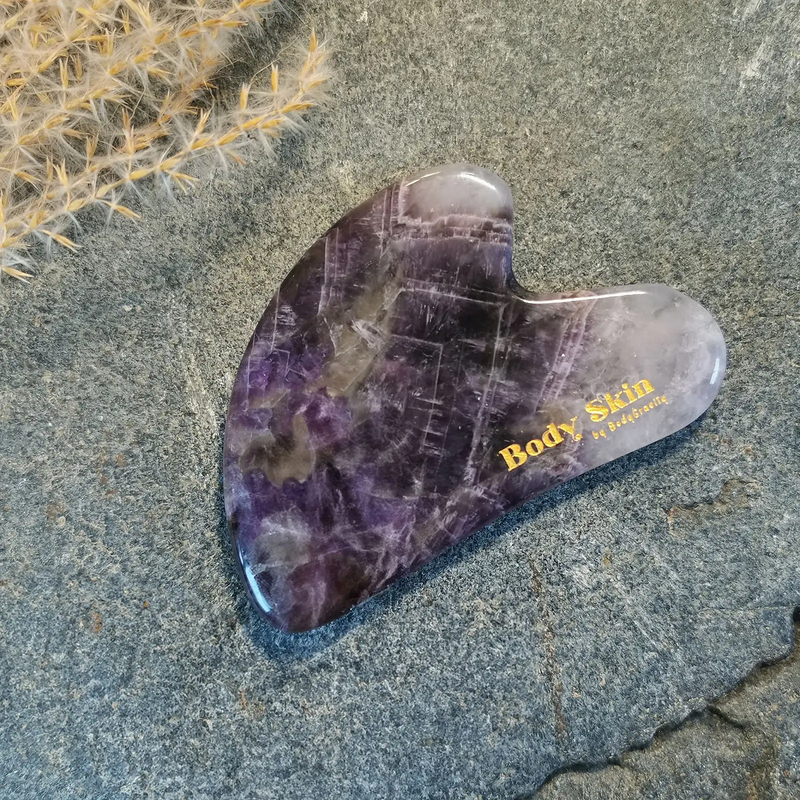 Zoom sur une pierre de gua sha améthyste disposée sur une pierre de granit
