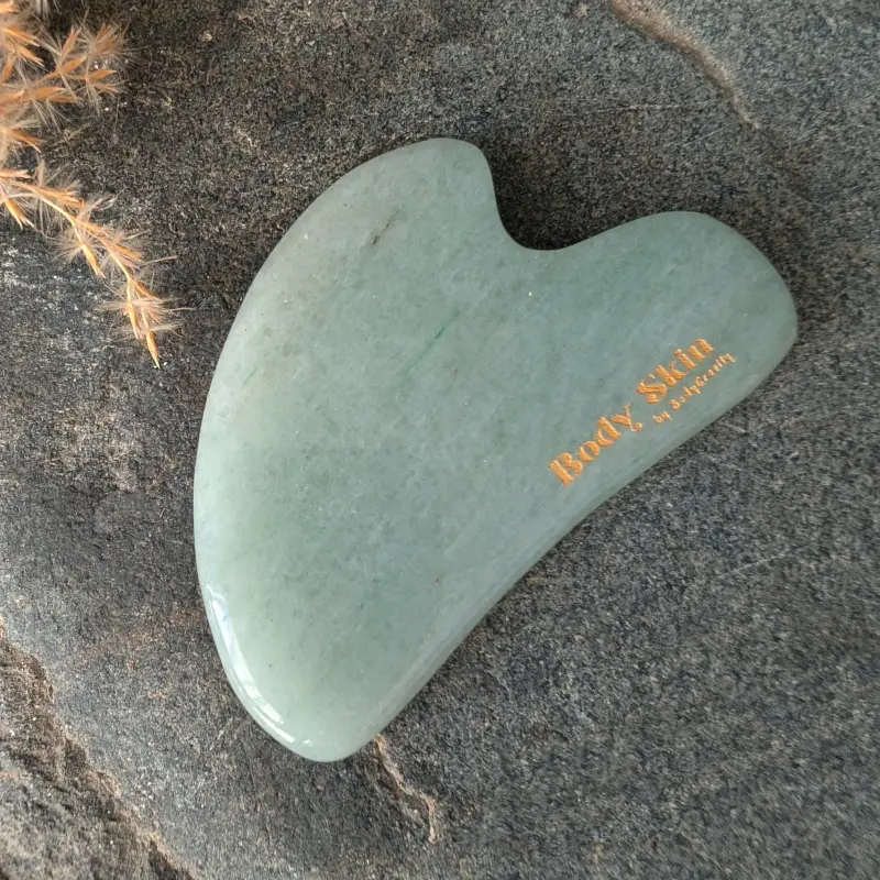 Zoom sur une pierre de gua sha aventurine disposée sur une pierre de granit