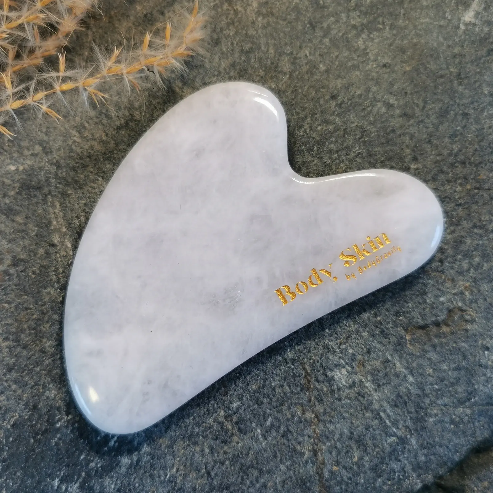Zoom sur une pierre de gua sha jade blanche disposée sur une pierre de granit