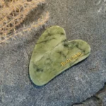 Zoom sur une pierre de gua sha jade verte disposée sur une pierre de granit