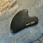 Zoom sur une pierre de gua sha obsidienne disposée sur une pierre de granit