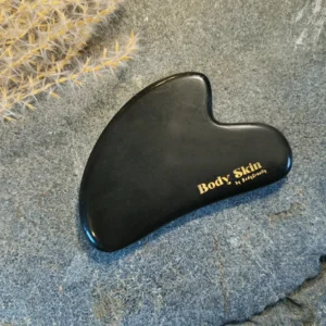 Zoom sur une pierre de gua sha obsidienne disposée sur une pierre de granit