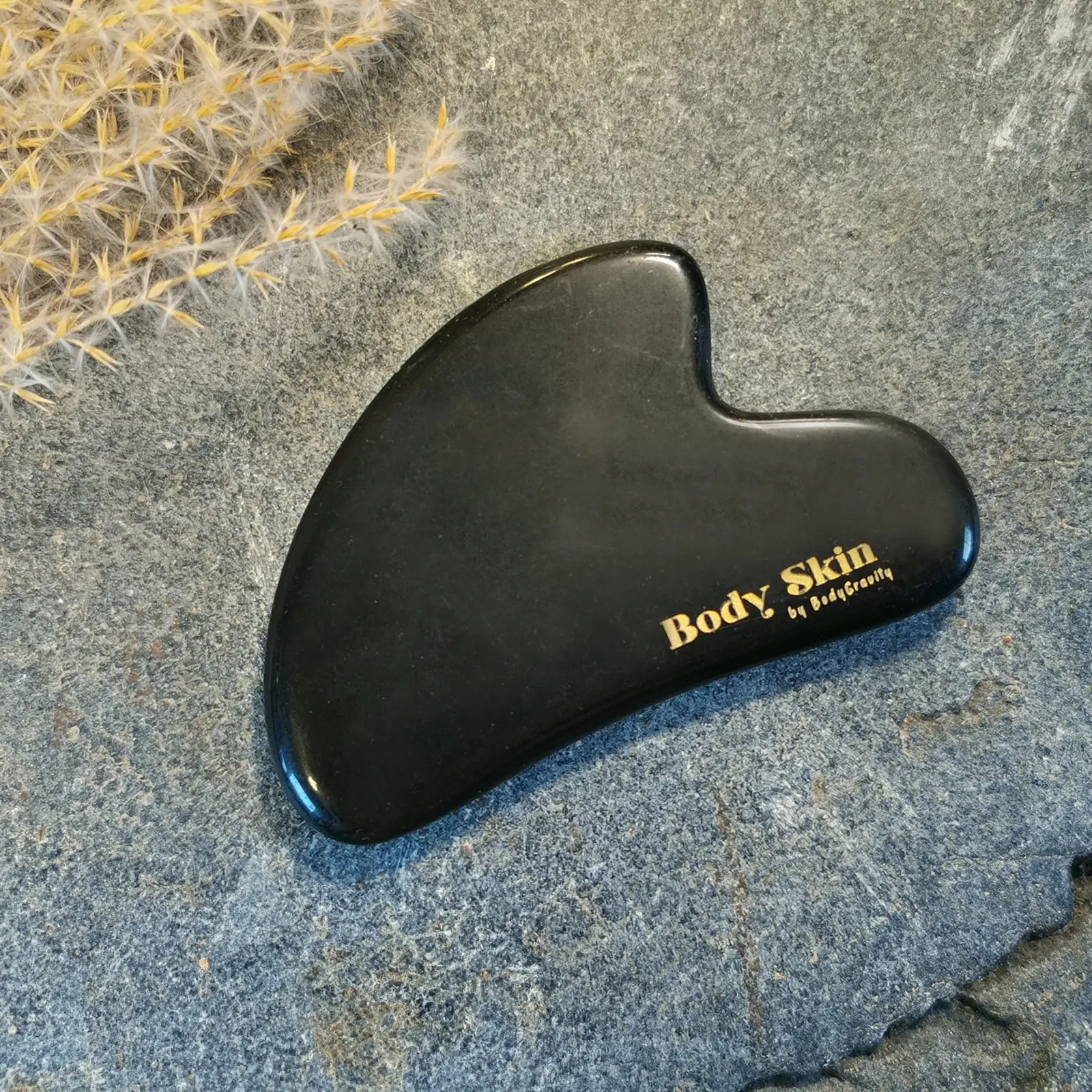 Zoom sur une pierre de gua sha obsidienne disposée sur une pierre de granit